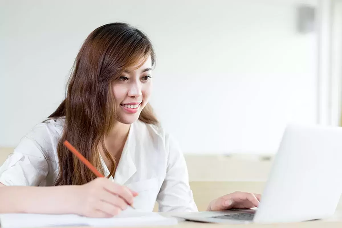Happy student looking at laptop and taking notes in journal