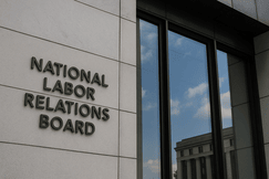 Exterior of the National Labor Relations Board headquarters building, showing the agency’s name mounted on a modern stone facade beside large reflective windows.