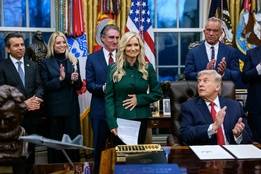 White House signing ceremony as senior administration officials applaud behind the president at the Oval Office desk.