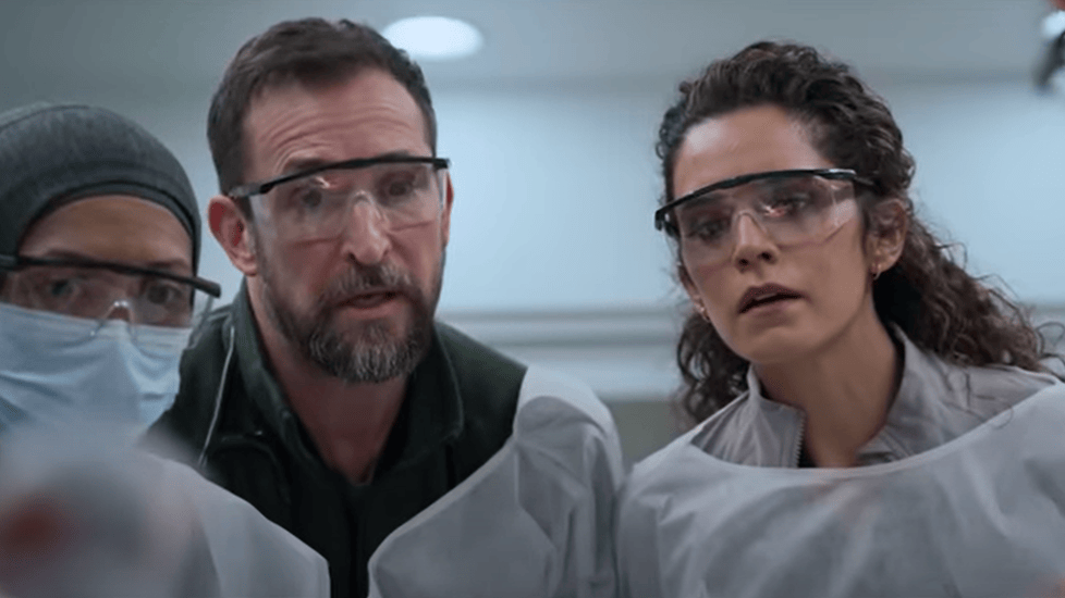 A group of healthcare professionals in protective gowns closely focused in a hospital setting, indicating a critical or intense moment in an emergency room environment.