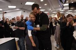 Noah Wyle and Katherine LaNasa embrace, celebrating The Pitt's 13 Emmy nominations while the cast and crew, dressed in hospital scrubs, gather in a brightly lit breakroom to cheer them on.