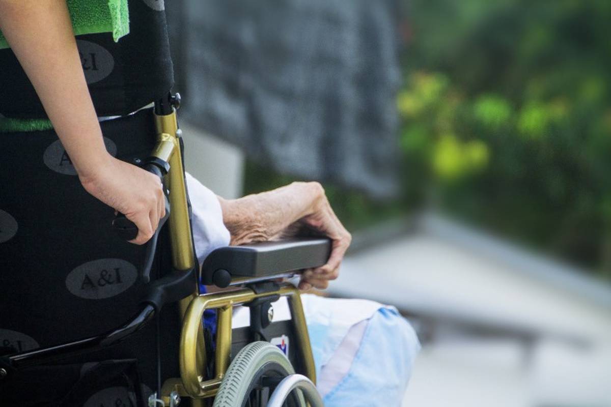 Woman helping elderly person by pushing wheelchair
