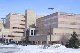 Exterior winter view of Alaska Regional Hospital and Alaska Medical Building in Anchorage, Alaska, with snow-covered ground, parked cars, and a sign reading ‘Alaska Regional’ in front of the campus.