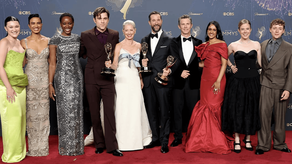 The cast and creators of 'The Pitt' pose together on the red carpet at the Emmy Awards, holding multiple trophies. The group is dressed in formal gowns and suits, standing in front of an Emmy backdrop