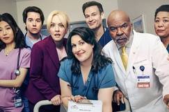 The cast of St. Denis Medical poses in a hospital hallway, dressed in scrubs and lab coats, capturing the show’s comedic hospital vibe.