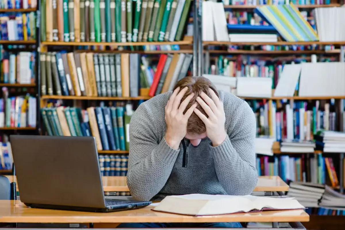 Man studying in library holding head in his hands