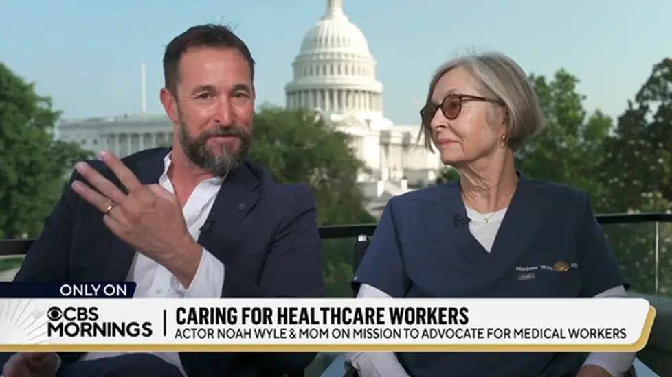 Actor Noah Wyle gestures while seated next to his mother, Marjorie Wyle-Katz, a nurse, during a CBS Mornings interview with the U.S. Capitol building visible in the background.