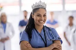 A portrait photograph shows a smiling nurse in blue scrubs wearing a stethoscope and an ornate silver tiara, with blurred hospital colleagues in the background.
