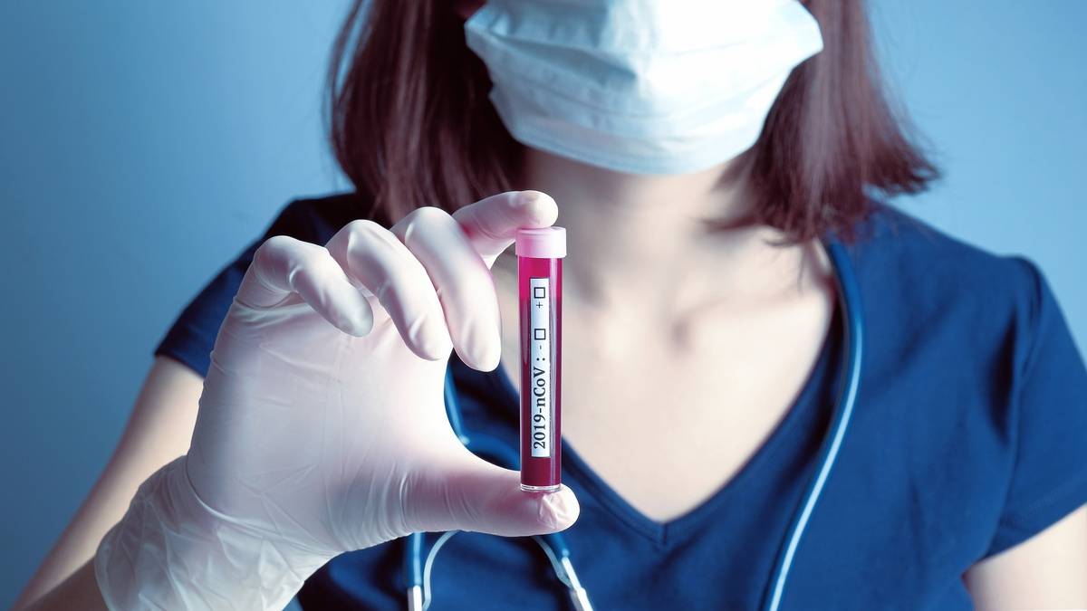 Nurse wearing respirator mask holding in hand test tube with patient blood for 2019-nCoV biochemical analysis