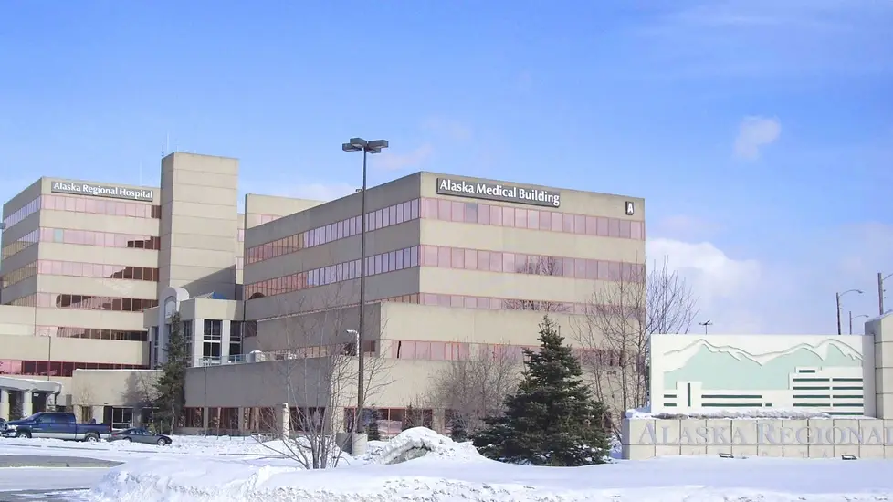 Exterior winter view of Alaska Regional Hospital and Alaska Medical Building in Anchorage, Alaska, with snow-covered ground, parked cars, and a sign reading ‘Alaska Regional’ in front of the campus.