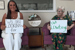 A nurse and an older woman sit holding signs that read “We are looking for…” and “Hot Cowboys” at Gainesville Health Care Center.