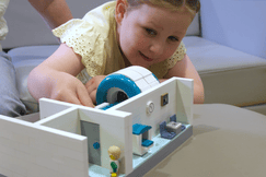 A young girl plays with a LEGO MRI scanner model, learning about medical scans through play.