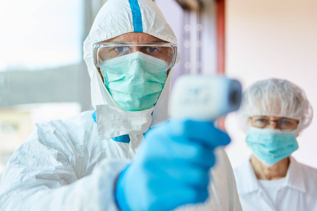 Two healthcare workers wearing PPE and taking patient's temperature