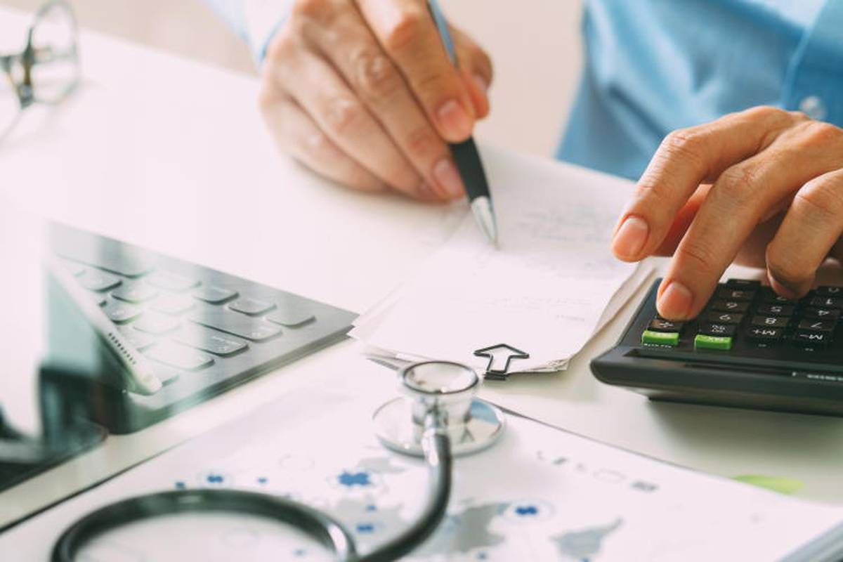 Doctor with stethoscope writing and using calculator