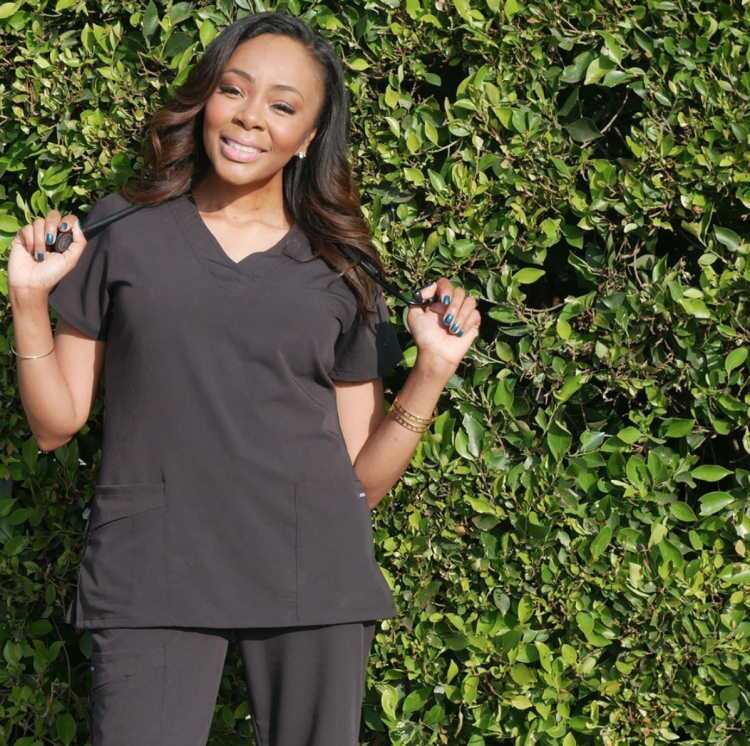 Nurse Alice posing with stethoscope in front of green hedge